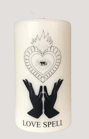 Bougie votive Mahala Love Spell ou sort d'amour. Bougie fabriquée en Italie. Bougie décorée d'une image d'un coeur sacré, d'une image de main en offrande, et de l'oeil de la connaissance. 60 heures de combustion. Bougie très belle en décoration. Bougie blanche et dessin noir. Bougie artisanale vendue sur l'eshop du magasin Lupinette Belgique et dans les boutiques Lupinette Bruxelles, Lupinette concept store Saint-Gilles, magasin Lupinette Uccle, boutique indépendante Lupinette Ixelles.  