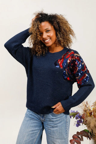 Pull bleu avec des sequins de multiples couleurs sur l'épaule gauche.