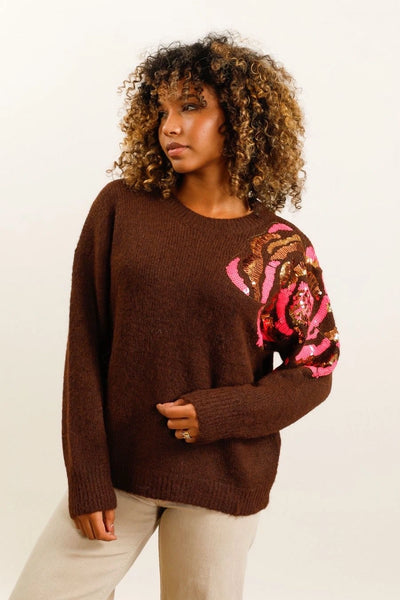 Pull marron avec des sequins de multiples couleurs sur l'épaule gauche.